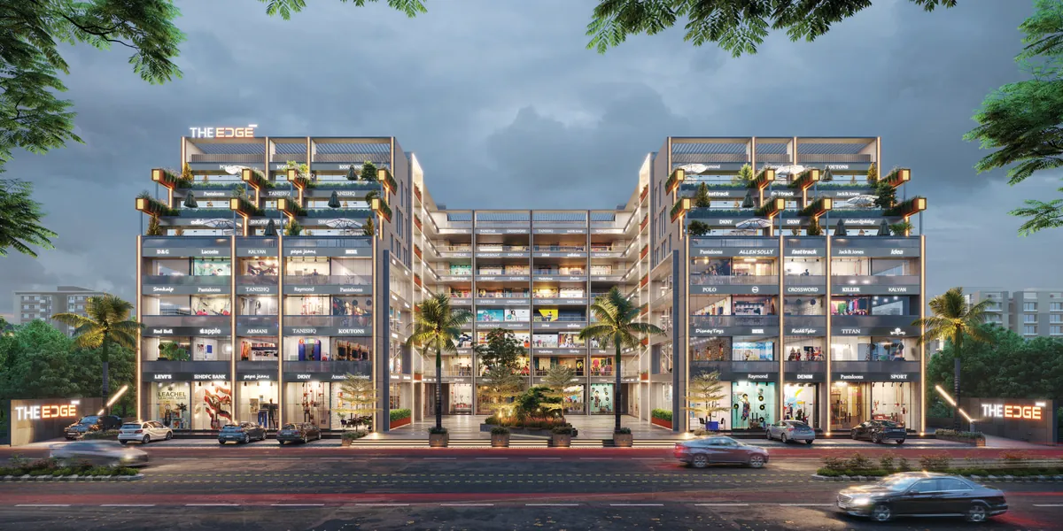 THE EDGE at night: twin retail and office blocks with lit shopfronts along the road